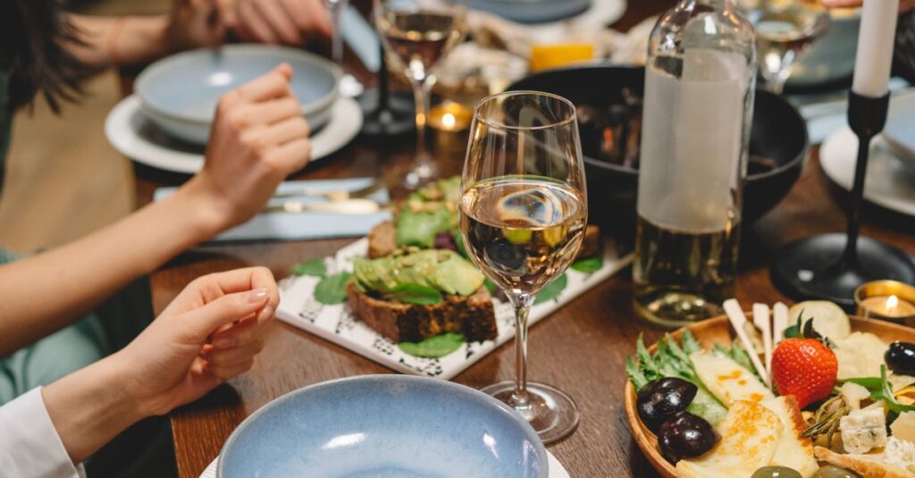 Close-up of a dinner table with wine, appetizers, and people enjoying a meal in a cozy indoor setting.