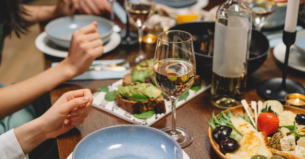 Close-up of a dinner table with wine, appetizers, and people enjoying a meal in a cozy indoor setting.